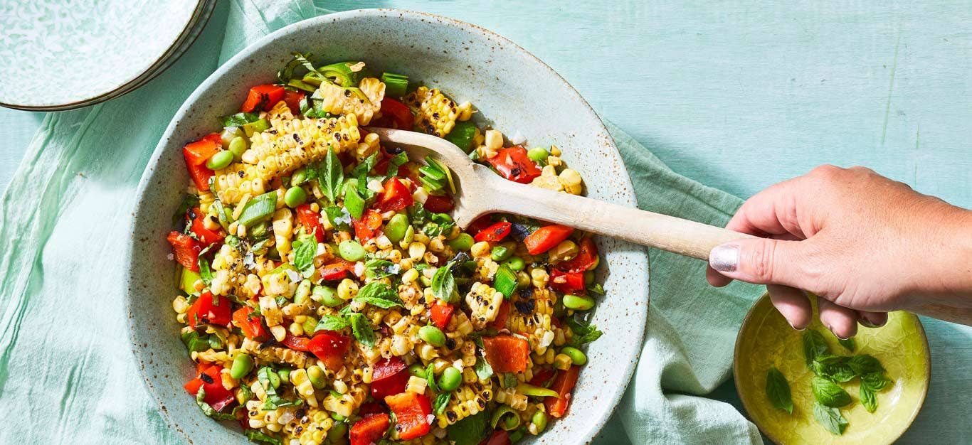 Grilled Corn Succotash in a ceramic bowl with a wooden spoon stirring the mixture