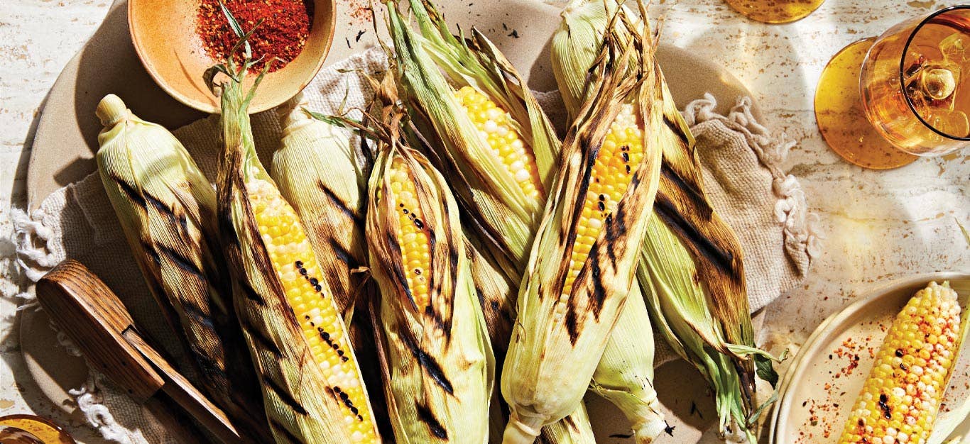 Perfectly Tender Corn on the Cob on a beige kitchen towel with a bowl of red seasoning