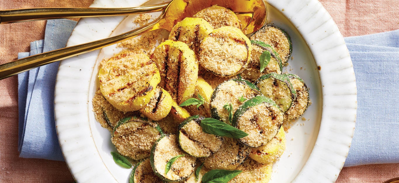 Grilled Summer Squash with Seasoned Bread Crumbs on a white plate with gold metal serving spoons