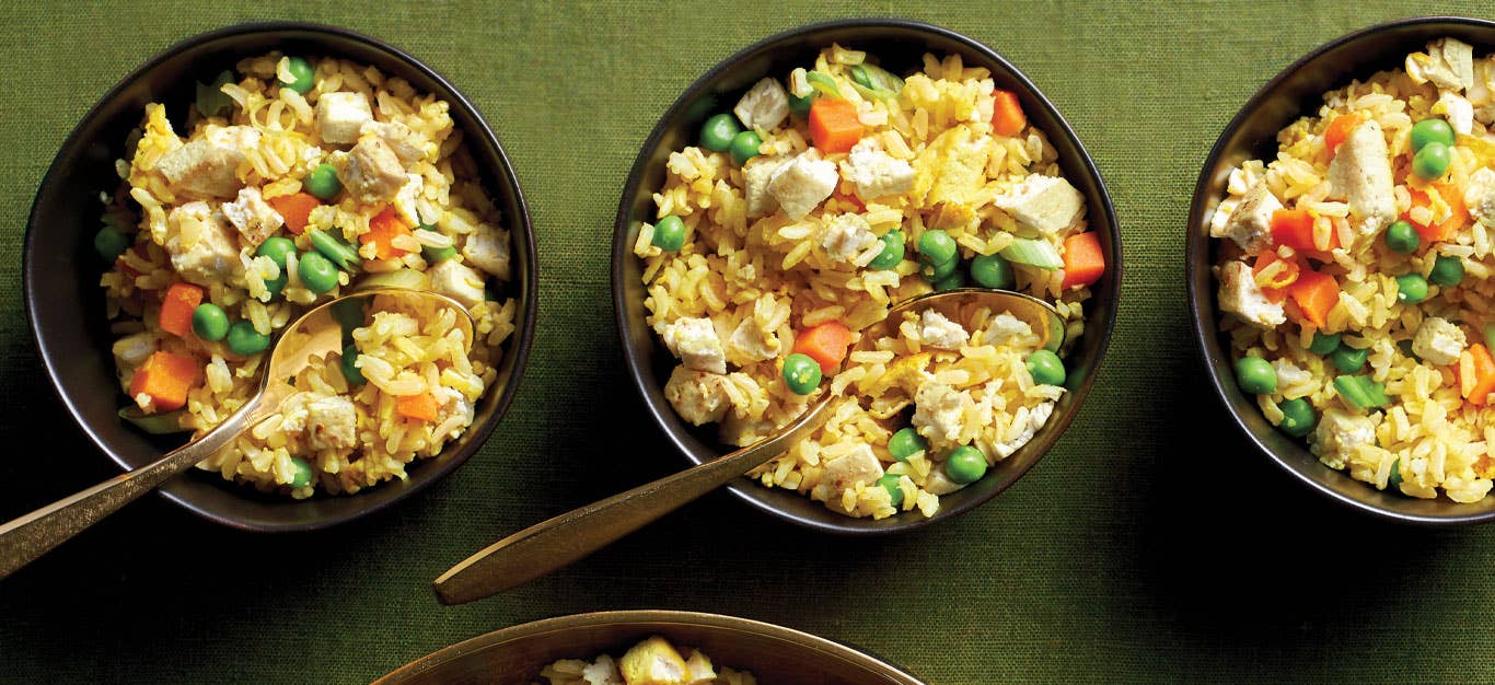 Oil-Free Tofu Fried Rice in small black bowl with metal spoons against a green tablecloth