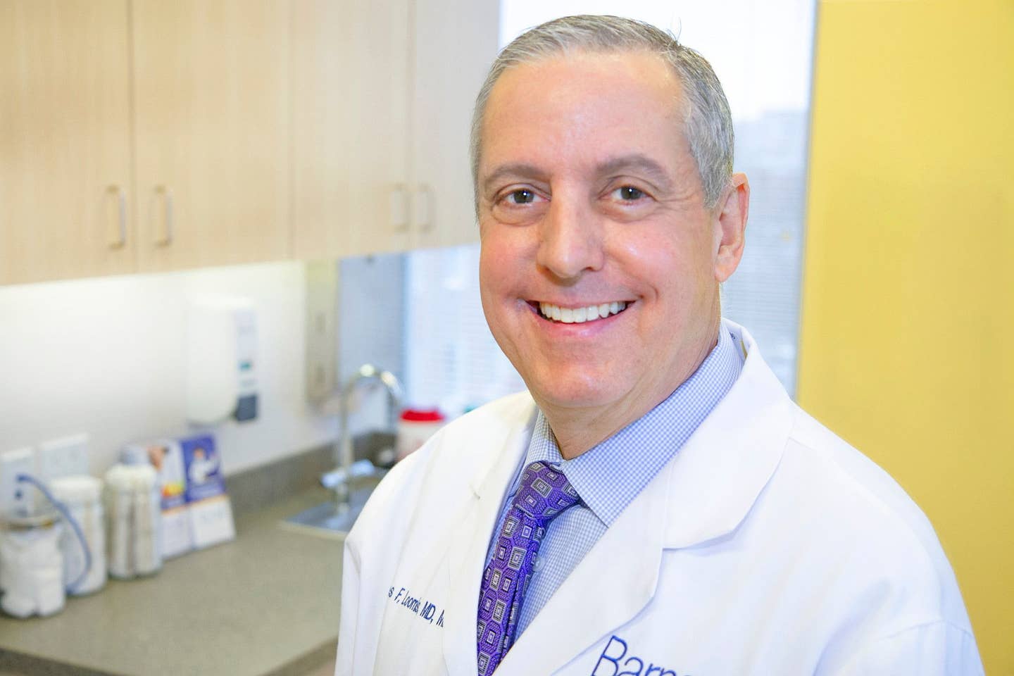 James Loomis Jr., M.D., M.B.A (1) Dr. James Loomis wearing a lab coat standing in an exam room