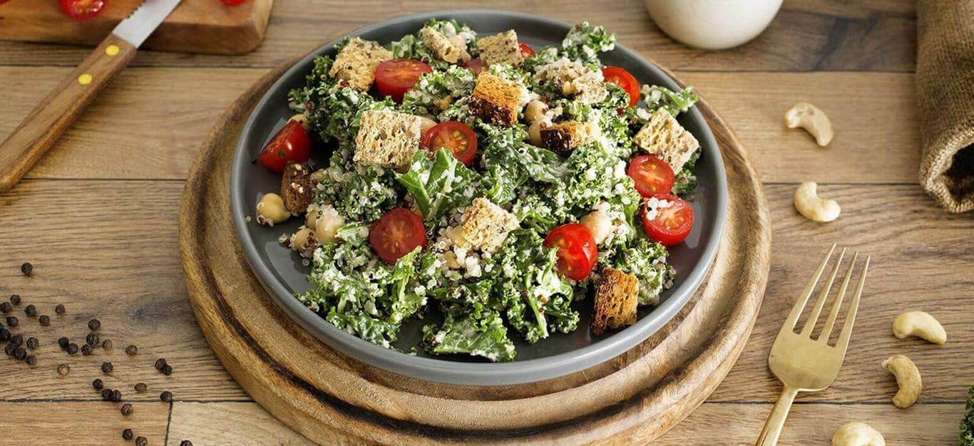 Vegan Kale Caesar Salad in a wooden bowl topped with croutons and tomatoes
