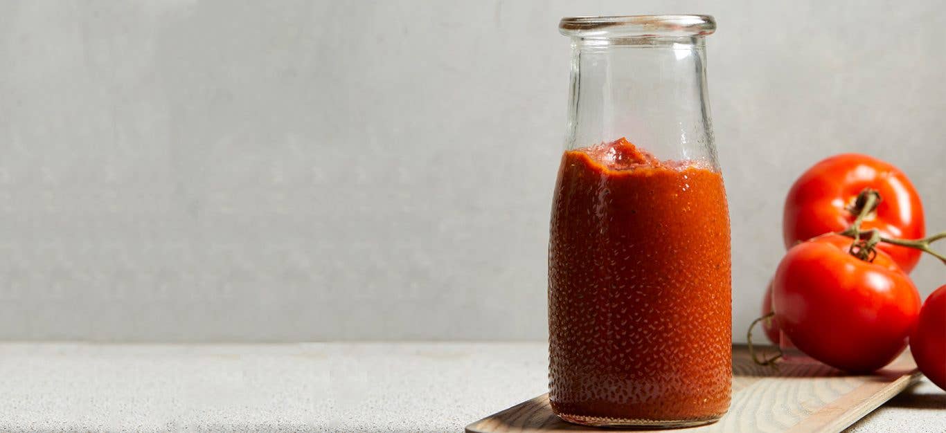 Homemade Ketchup in a glass bottle sitting on a wood cutting board next to fresh tomatoes