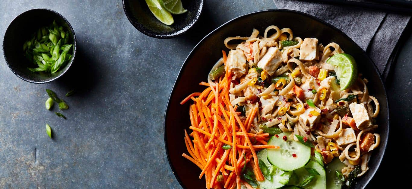 Pad Thai with Tofu sprinkeld with carrots and cucumbers in a large black bowl