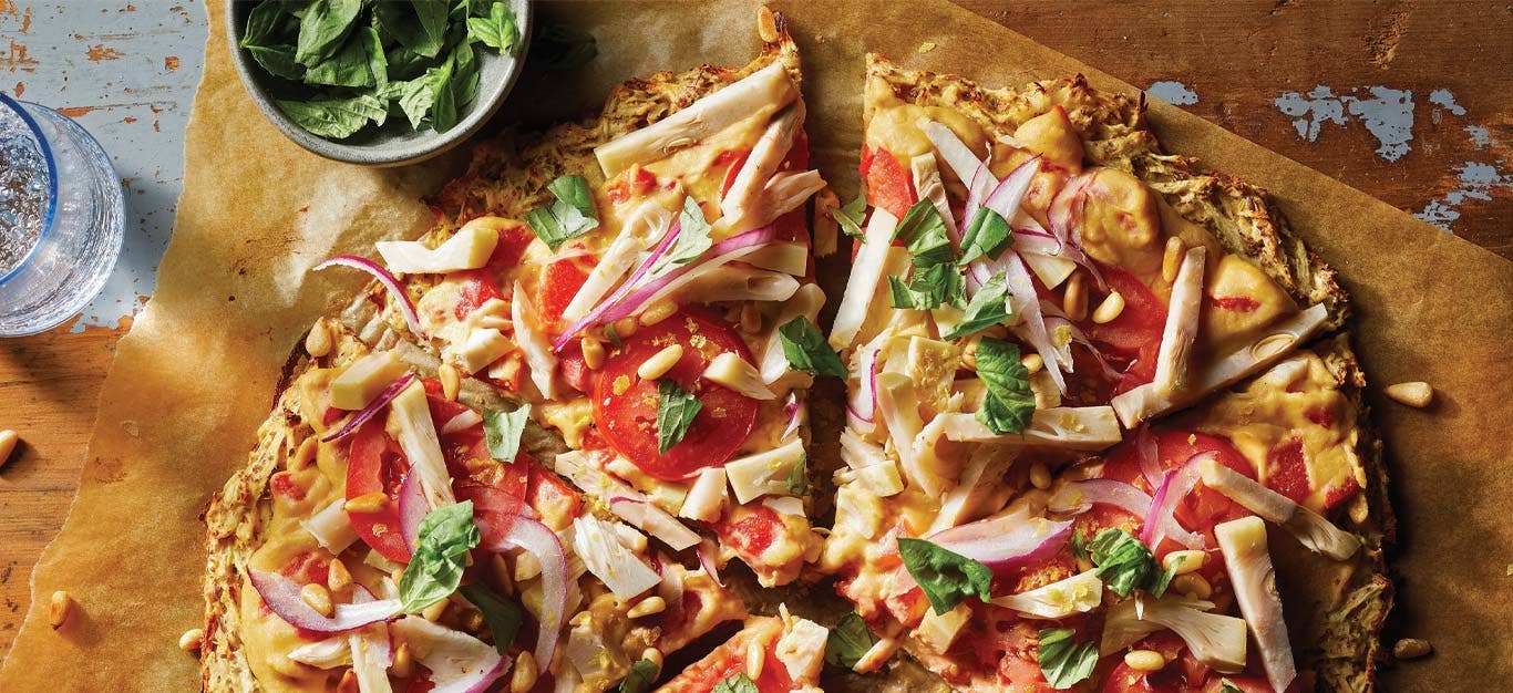 Parsnip-Crust Veggie Flatbread on parchment paper next to a small bowl of basil leaves