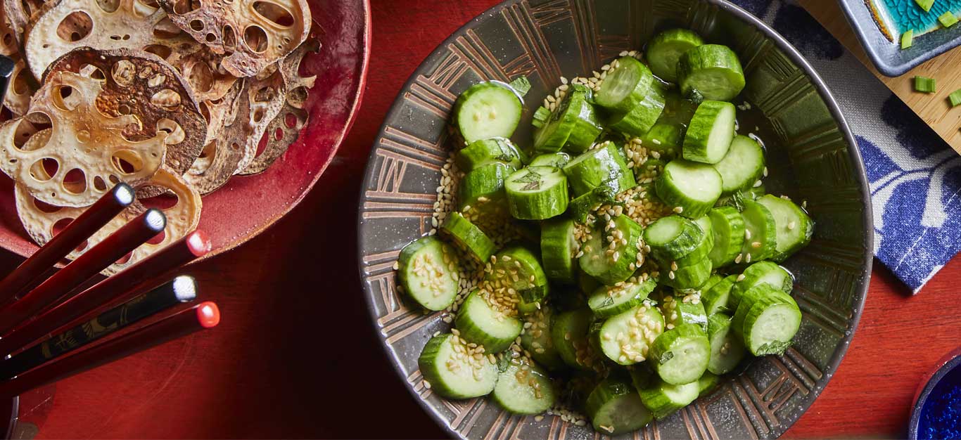 Quick-Pickled Japanese Cucumbers in a ceramic dish on a red table with lotus chips in the corner