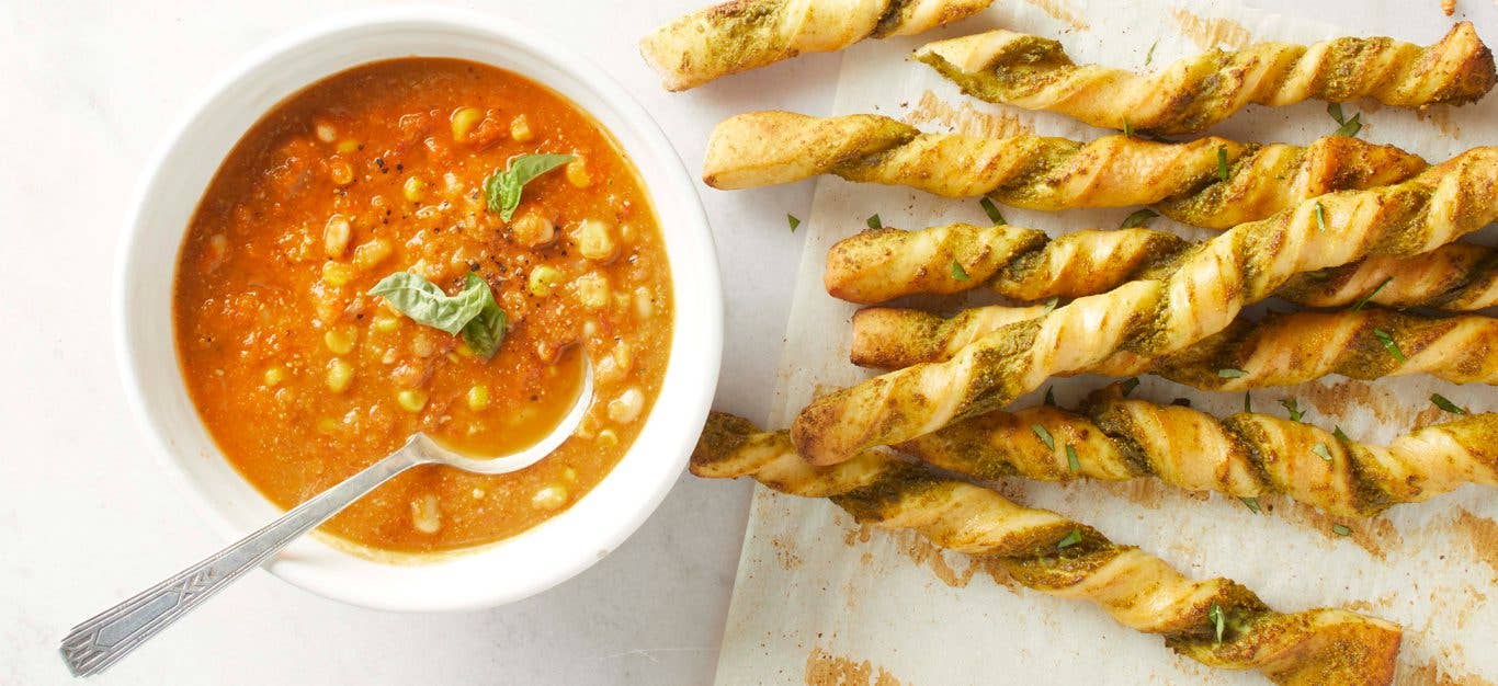 A bowl of Summer Tomato Soup with Pesto Breadsticks on the side