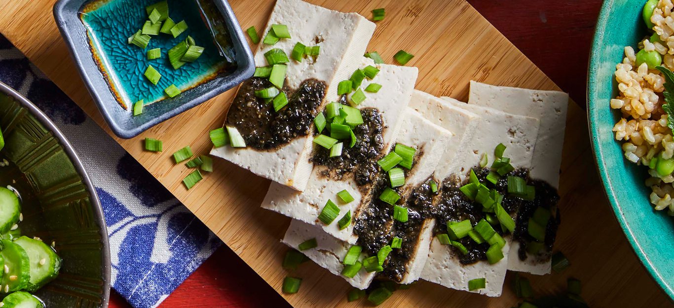 Soft Tofu with Black Sesame and Wasabi Sauce on a wooden cutting board and sprinkled with scallinos