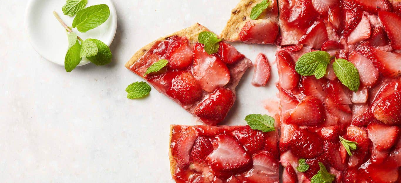 Strawberry Dessert Pizza sprinkled with fresh mint leaves on a white marble countertop