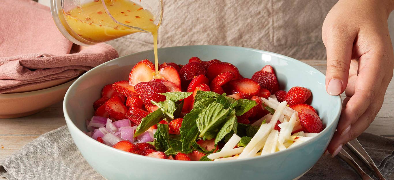 Strawberry-Mint Salad with Easy Maple-Dijon Dressing in a light blue ceramic bowl with a woman's hand holding the right side of the bowl