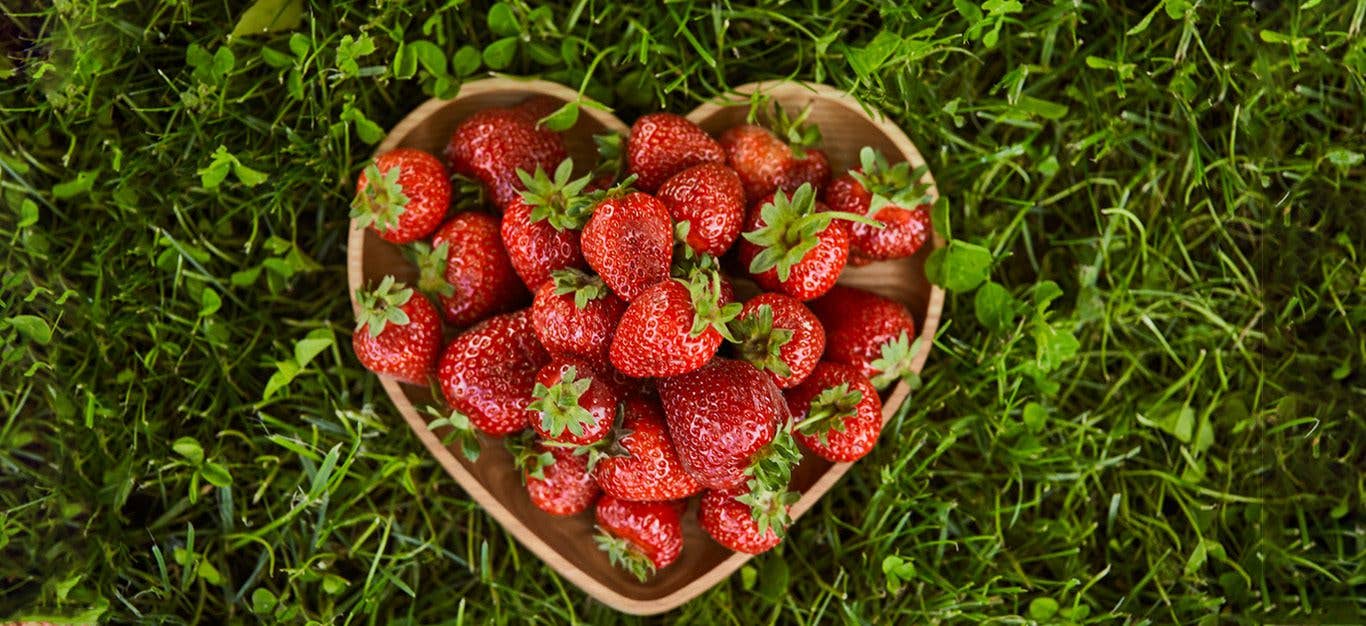 A heart-shaped bowl of strawberries set on green grass