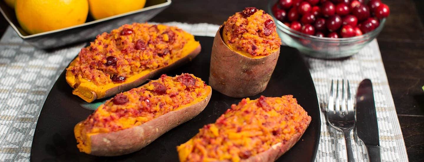 Twice Baked Sweet Potatoes on a black plate. In the background is a bowl of fresh cranberries and a bowl of oranges