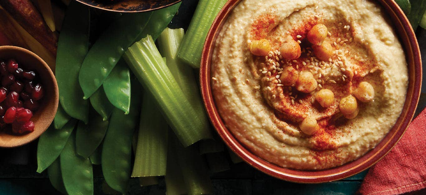 Low-Fat Hummus in a red bowl next to celery sticks and snap peas