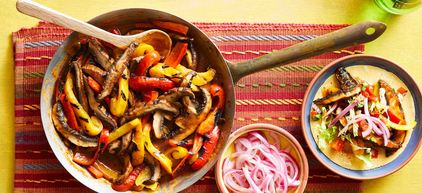 Vegan Barbacoa Fajitas on a red and yellow striped placemat with a bowl of pickled onions