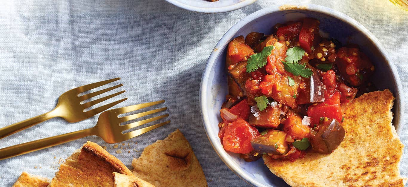 Warm Spiced Eggplant Salad in a small blue bowl with a side of pita bread