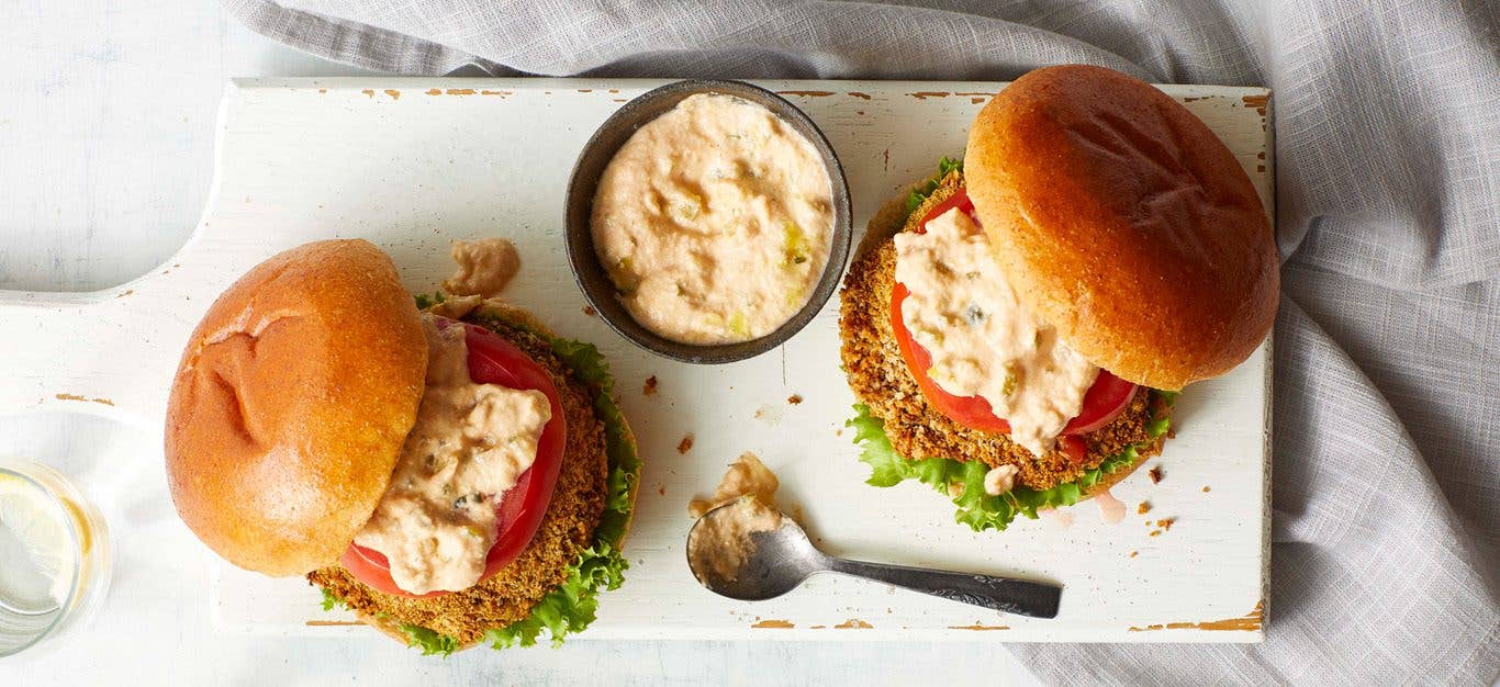 Two breaded air-fryer portobello burgers shown from above, drizzled with Thousand Island dressing, which is also in a ramekin between the burgers