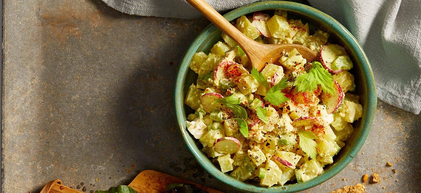 Vegan Egg Salad - Diced potatoes, celery, and other veggies and herbs shown tossed together for a vegan egg salad, in a green bowl on a concrete table