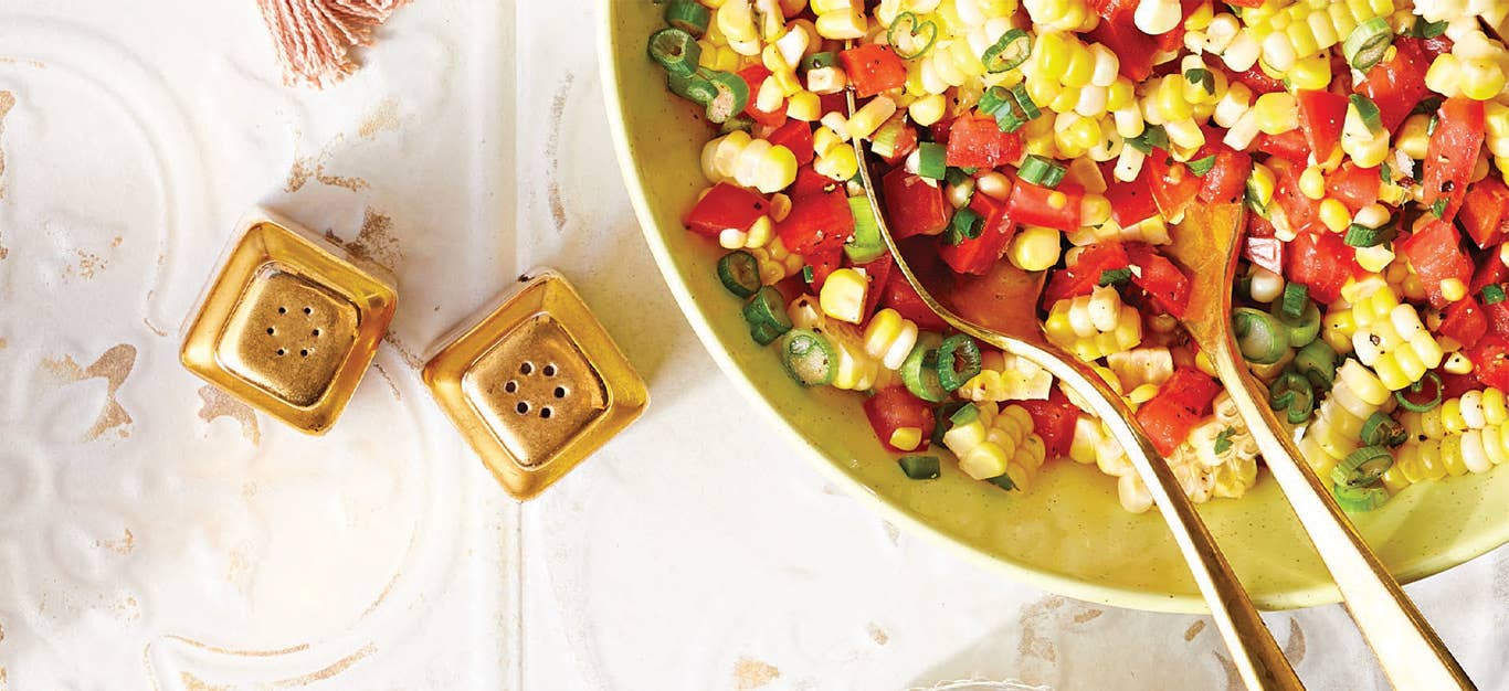 Spicy Corn and Tomato Salad in a yellow serving bowl with metal serving utensils