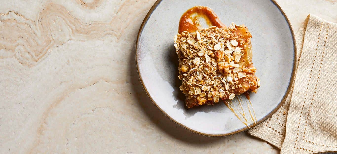 Vegan apple pie bar shown with a drizzling of cider glaze on a white dessert plate