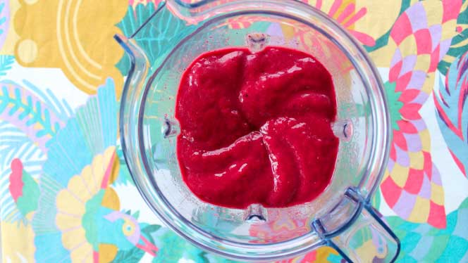 Top down view of smoothie in a blender on a colorful tablecloth