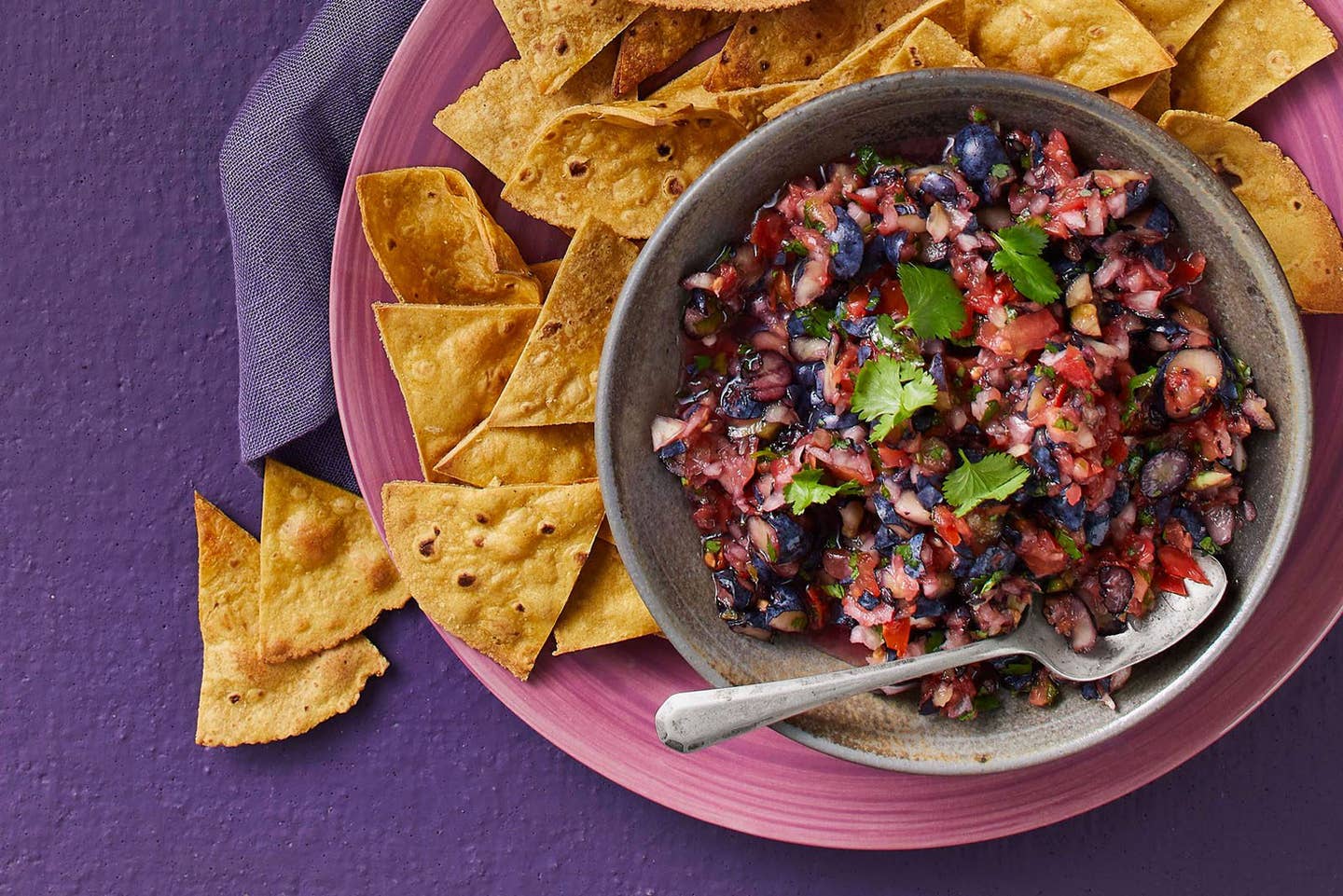 Blueberry salsa with tortilla chips on the side on a purple table