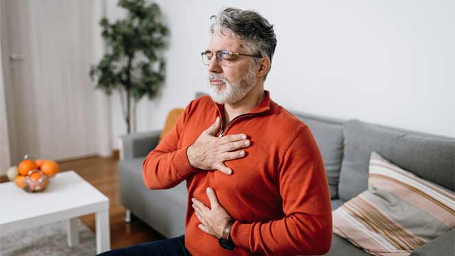 breathing exercise Older man in an orange sweater with a hand on his heart and a hand on his belly, breathing deeply