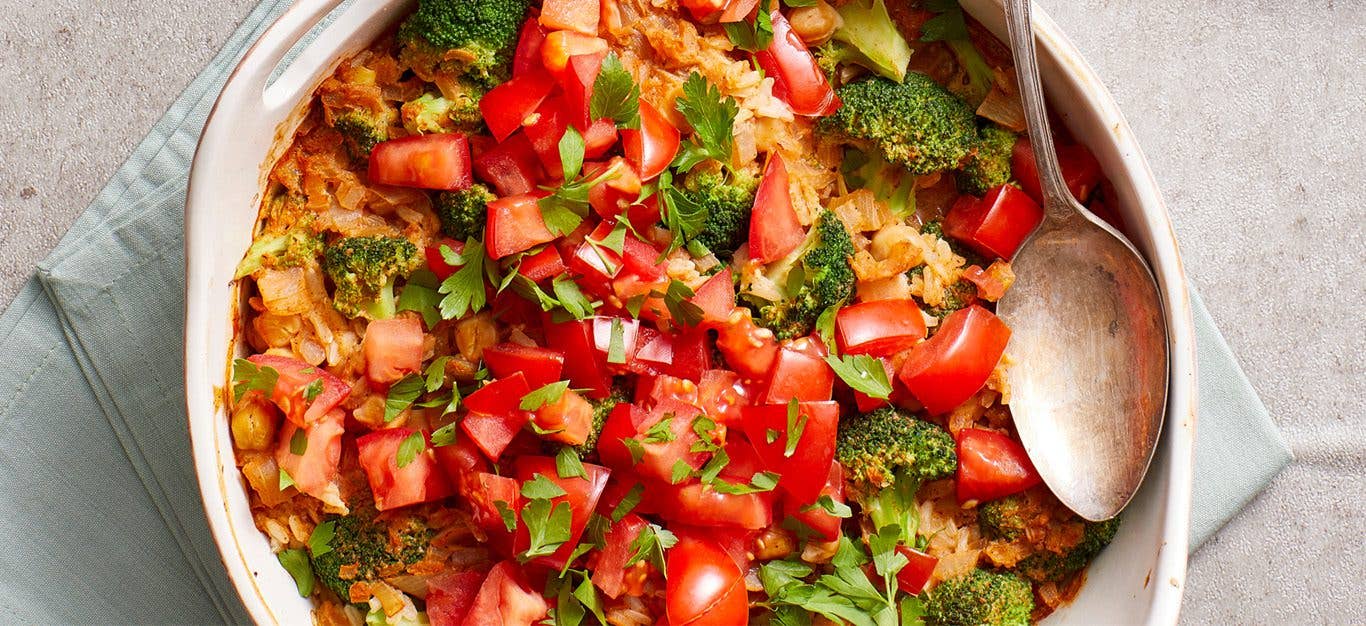 brown rice casserole with broccoli and tomatoes, shown in a round white casserole dish