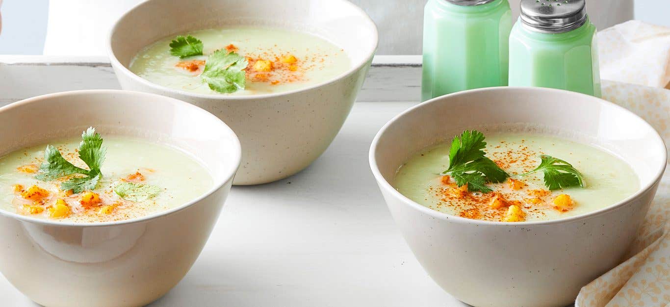 Three bowls of pale green-hued Chayote Soup with Roasted Hominy in white bowls