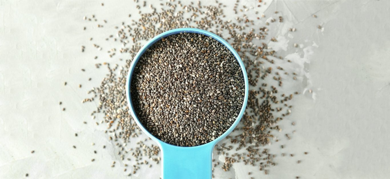 chia seeds in a blue bowl with a handle, with some spilling out underneath and around the bowl onto a gray background