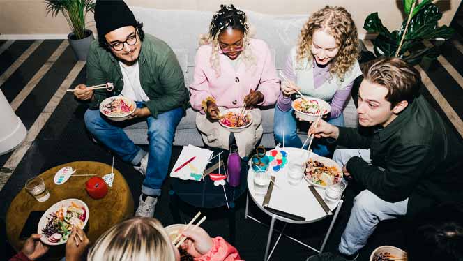 A group of college students sit in a circle eating veggie and rice bowls