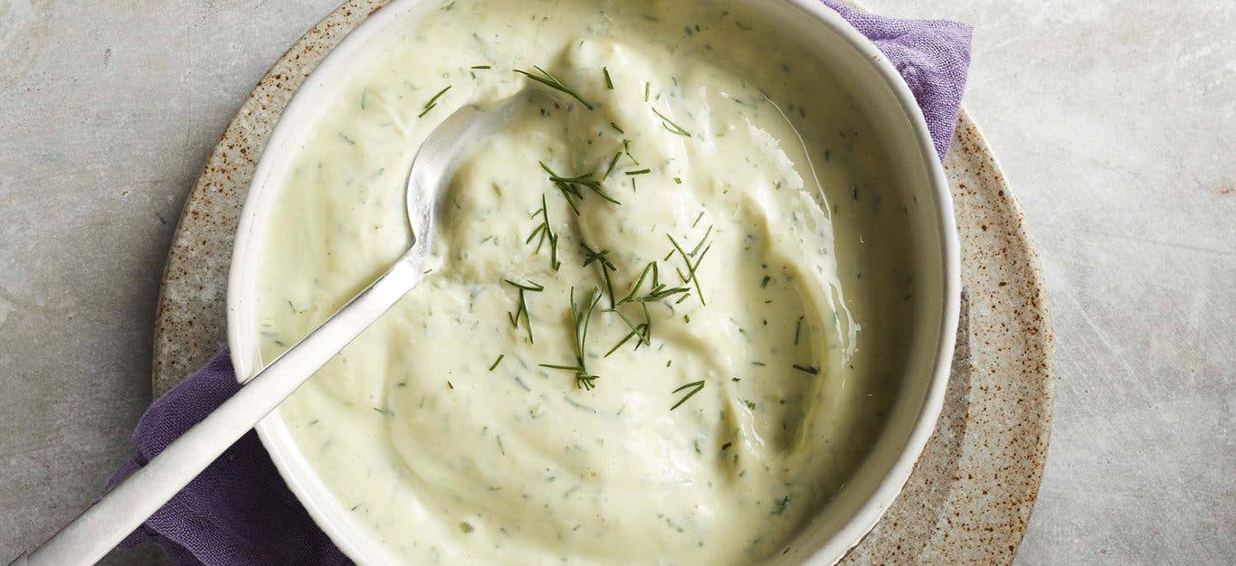 creamy dill dip in a white bowl with a metal spoon resting in the dip