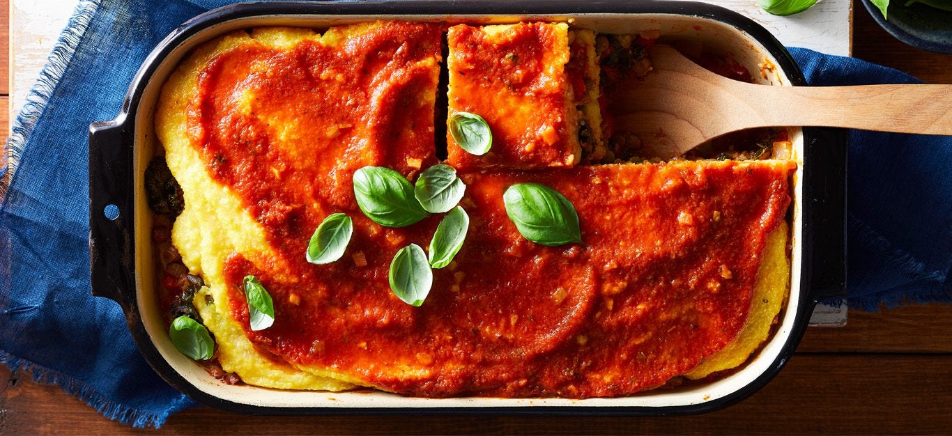 polenta lasagna casserole shown topped with marinara sauce and fresh basil leaves