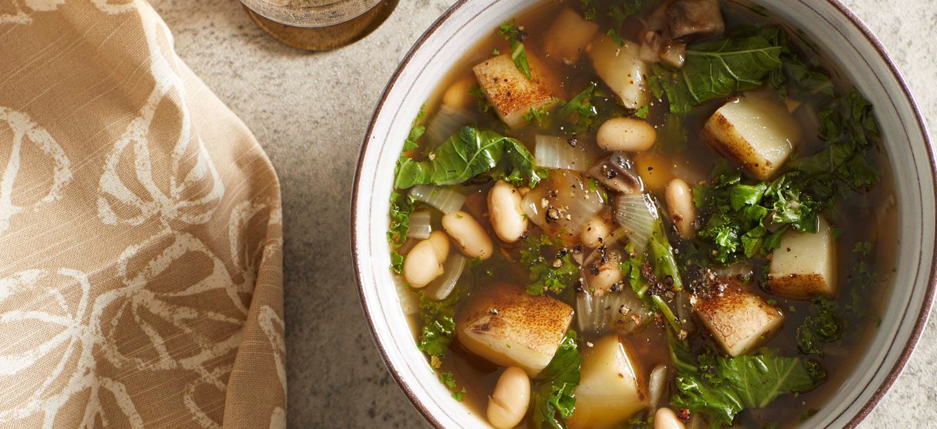 a bowl of minestrone with a thick broth, kale leaves, and chopped potatoes and white beans visible in soup