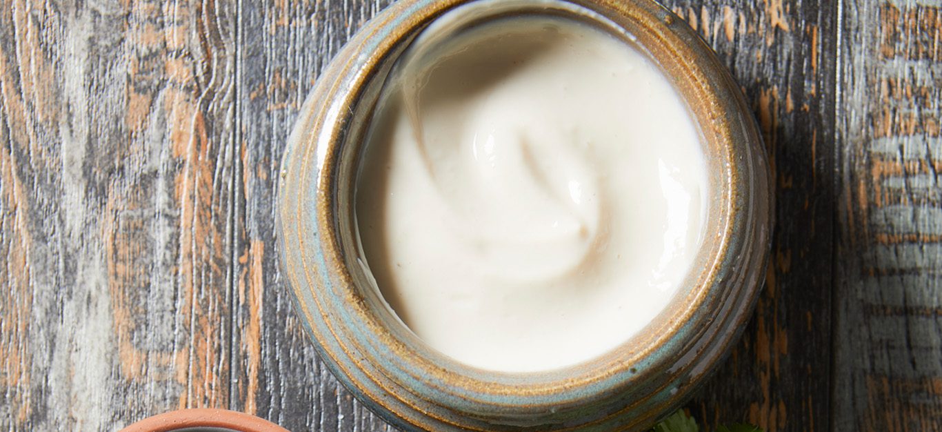 Vegan, plant-based mayo - light, fluffy looking white vegan mayo in a jar, shown from above, sitting atop a gray wooden table
