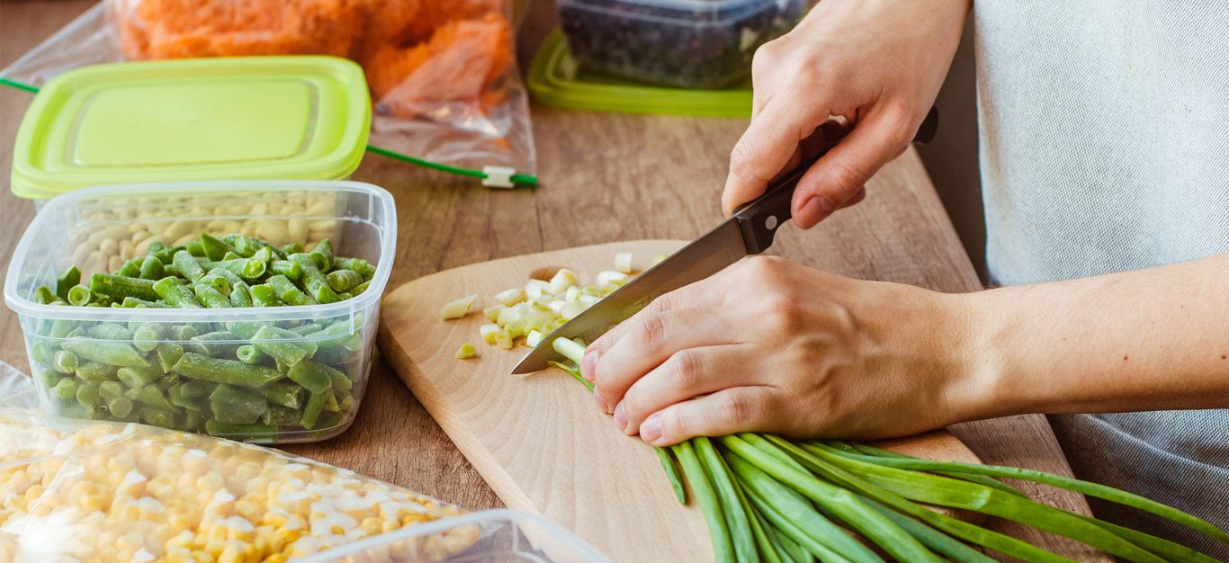 Woman chopping scallions on a wooden cutting board, with plastic tupperware containers beside for meal prep