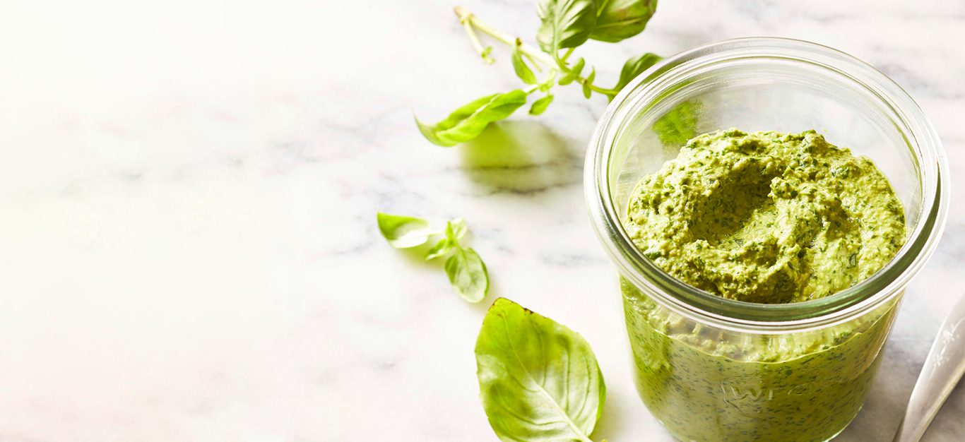 Homemade Vegan Pesto in a glass jar on a white marble table