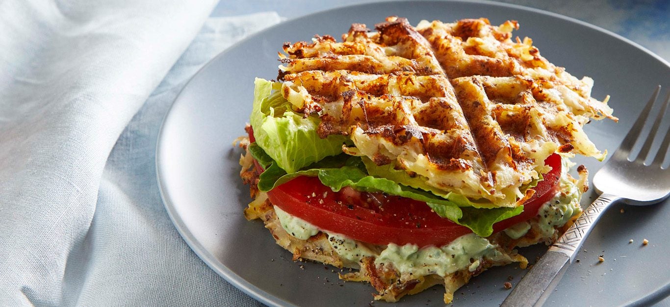 potato waffle sandwiches with lettuce, tomato, and herbed tofu cream on a gray plate with a fork