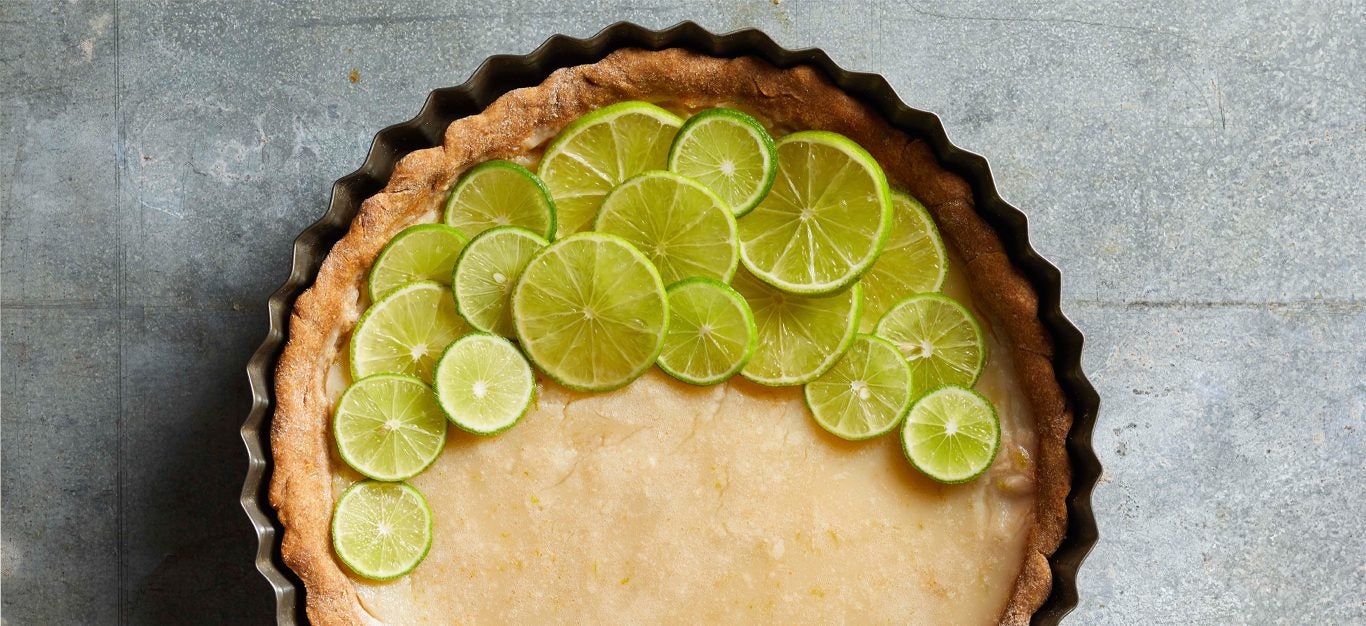 Vegan Key Lime Pie with fresh lime slices in a tart tin on gray marble counter