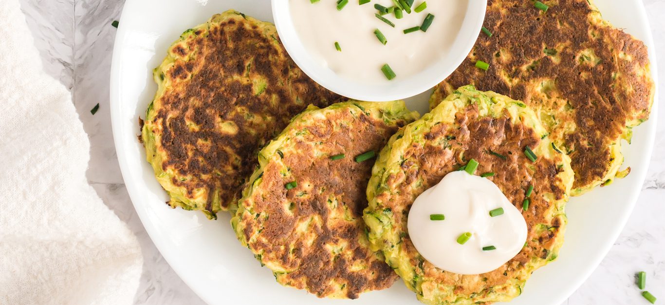 Zucchini Fritters with a dollop of vegan sour cream and chives on a white plate