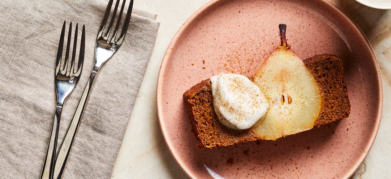 Gingerbread Loaf with Poached Pears topped with whipped cream on a pink plate