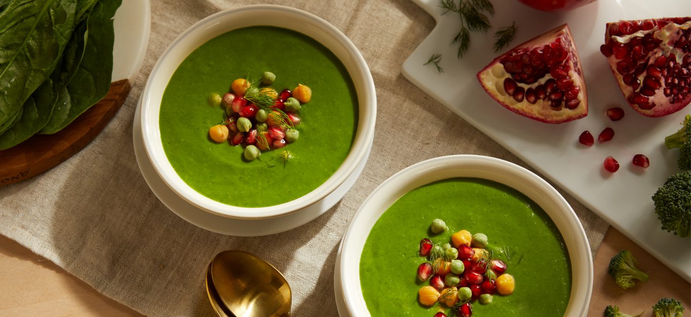Super Greens Soup with Chickpeas in white bowls next to an open pomegranate