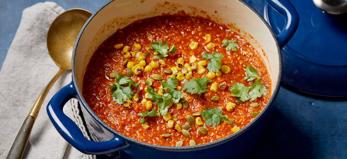 A bright-colored roasted red pepper stew, sprinkled with cilantro, in a blue pot