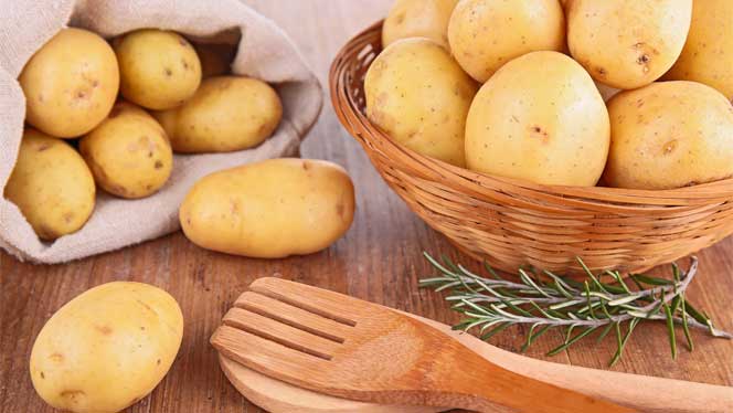 Potatoes in a wooden bowl with a sprig od rosemary and wooden utensils