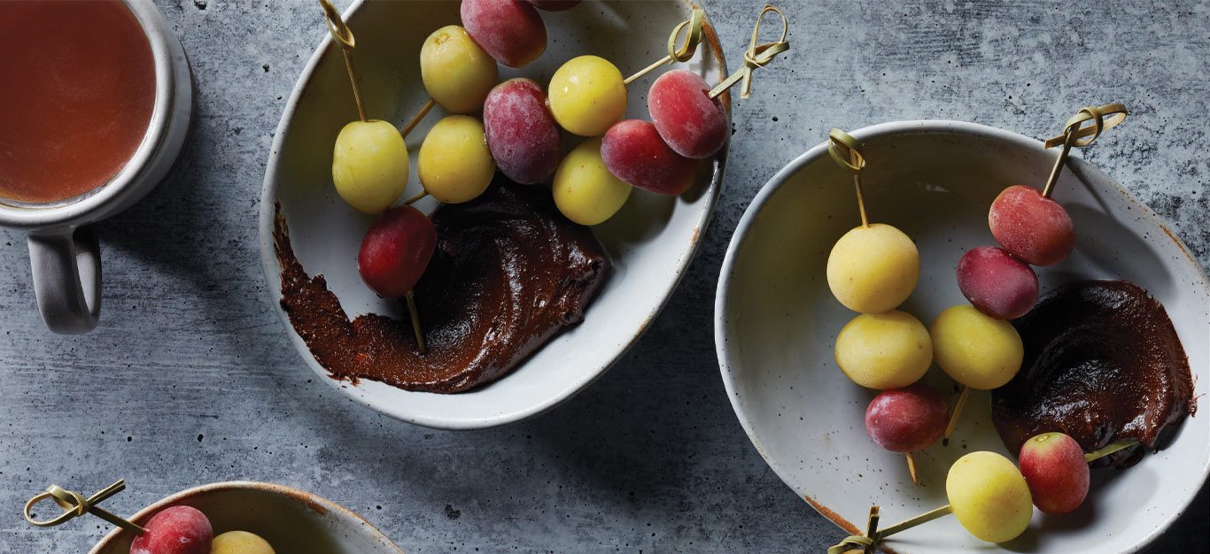 Frozen Grapes with Chocolate Sauce in light gray bowls with a cup of tea on the left