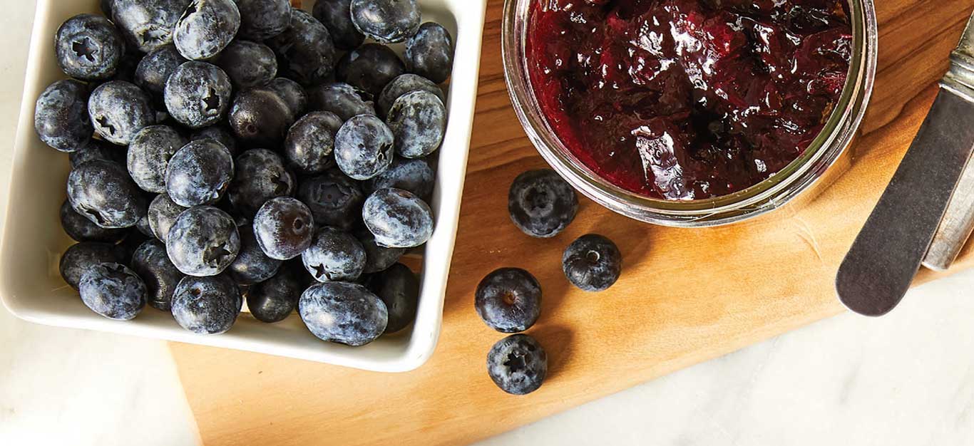 A small carton of blueberries beside a mason jar of homemade jam on a cutting board
