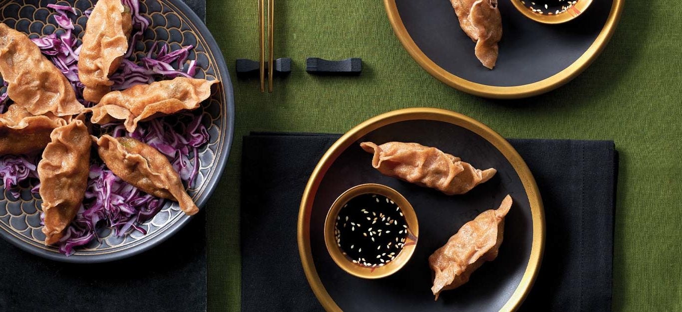 Sweet Potato and Shiitake Mushroom Dumplings on black and gold plates with a small bowl of soy sauce against a green tabletop