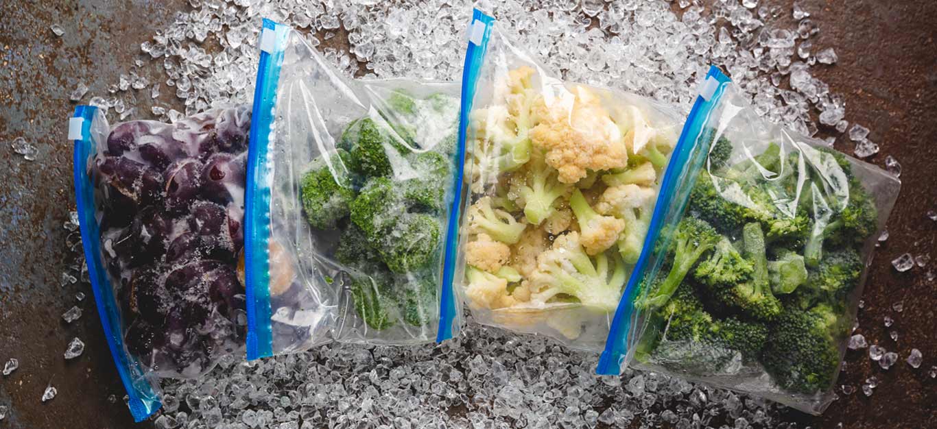 Frozen vegetables in zip-top bags on a table with tiny ice crystals surrounding them - airtight bags can help prevent freezer burn