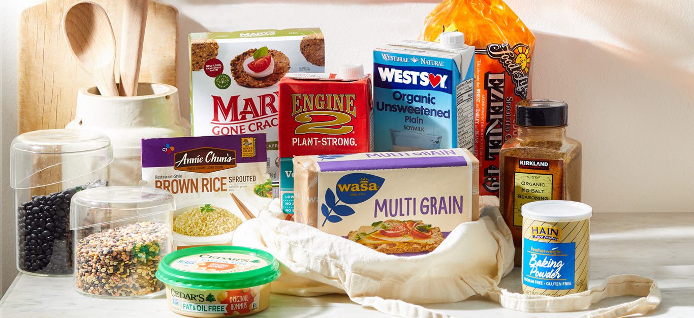 An array of oil-free vegan food products found at the grocery store, spread out on a kitchen counter, for whole-food, plant-based shoppers