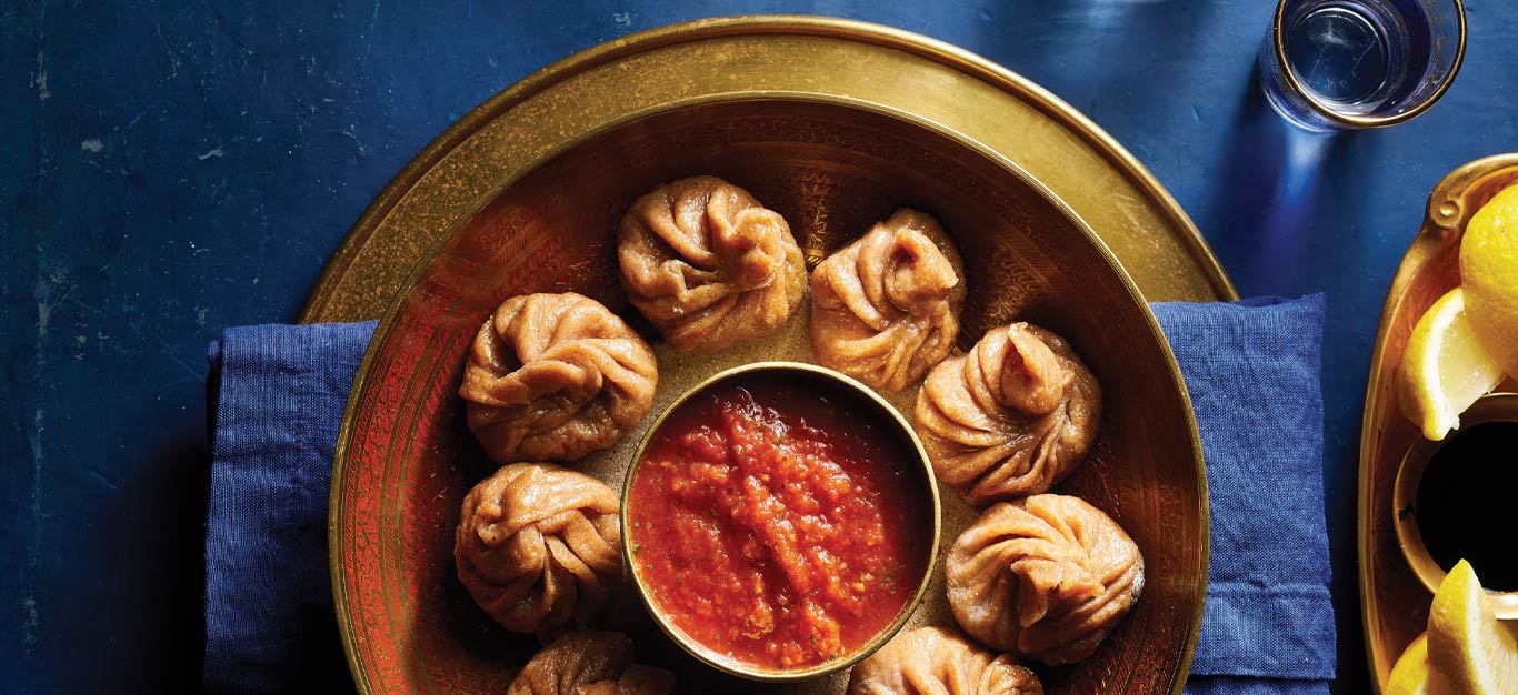 Tofu Vegetable Momos with Tomato Chutney on a gold metal plate on a dark blue tabletop