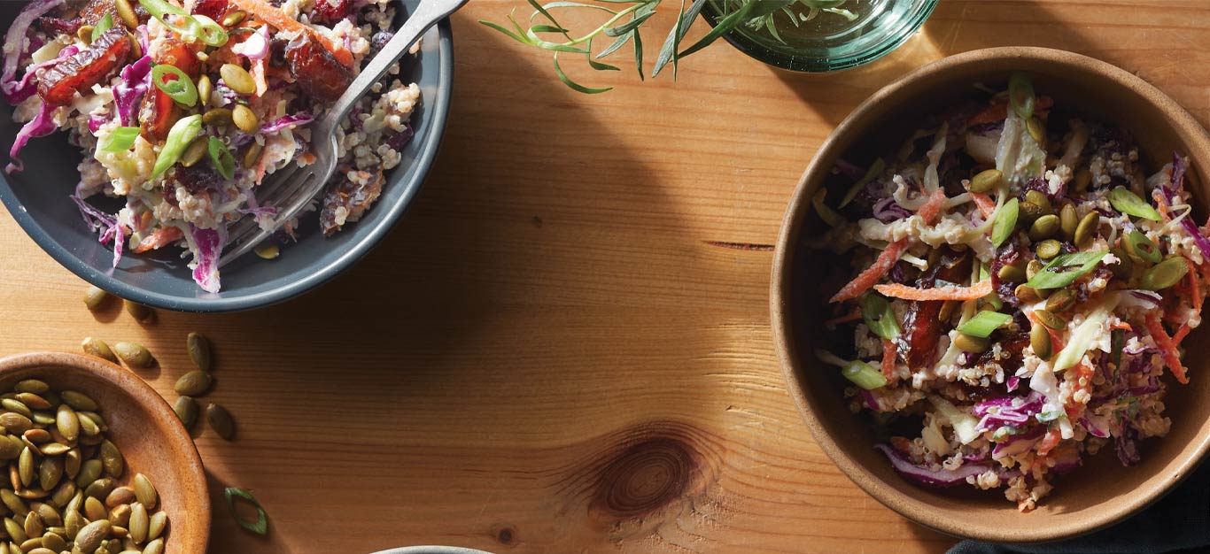 Hearty Winter Slaw with Quinoa and Cranberries in brown and blue bowls against a wood tabletop